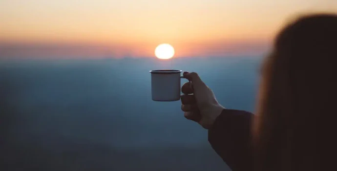 En hånd holder en kaffekop op mod solopgangen – symbol på Blind Coffee og at skabe sin egen vej.