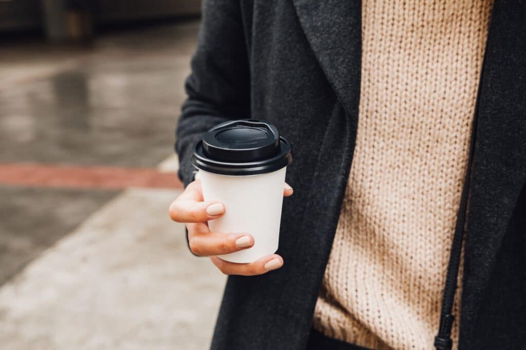 Female hand holding a coffee to go on the street.
